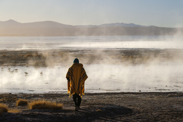 Person in ethnic clothing from the back next to a hot spring pool in the middle of the Bolivian...