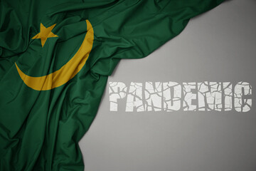 waving colorful national flag of mauritania on a gray background with broken text pandemic. concept.