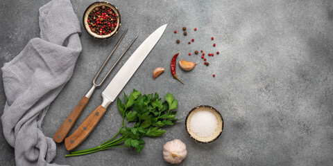 Cooking background, knife, meat fork, spices and greens. Gray concrete background. Top view, flat...