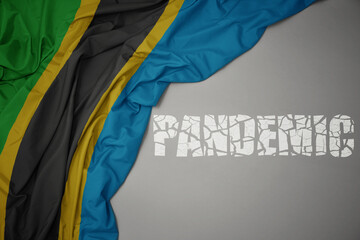 waving colorful national flag of tanzania on a gray background with broken text pandemic. concept.