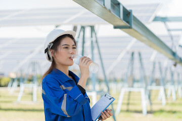 Female engineer worker drinking water during working in solar panels power farm. Technician working...
