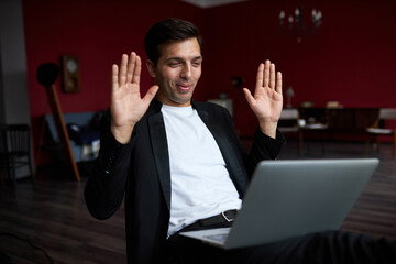Executive manager having video conference with partners at his office with laptop on knees, smiling...