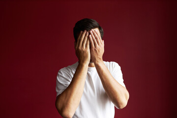 Desperate guy in white clothes hiding his face behind opened palms, feeling ashamed for mistake and...