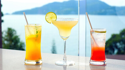 Three vibrant fruit margarita cocktails in colorful glasses, perfect for a summer getaway. Enjoy refreshing drinks by the pool with a sea view at a luxurious villa.