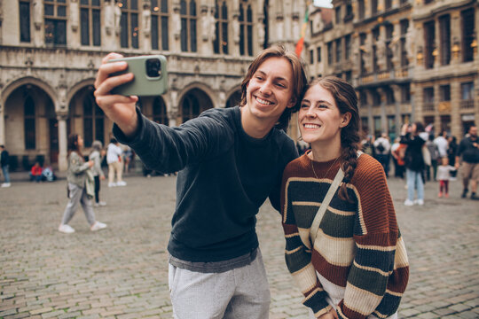 couple taking a selfie in front of a crowded town center in europe grand palace