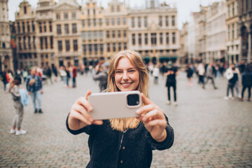 female traveler taking a selfie in front of a crowded town center in europe grand palace