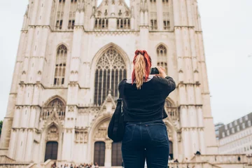 Gordijnen woman wearing a red kerchief taking a photo of a cathedral © kristineldridge