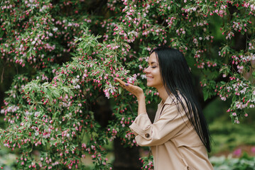 Caucasian young brunette woman sniffs the flowers of an ornamental apple tree in spring in the park