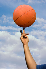 a basketball spinning on a finger with clouds in background