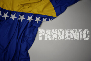 waving colorful national flag of bosnia and herzegovina on a gray background with broken text pandemic. concept.