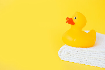 Stacked white towels and bath duck on yellow background