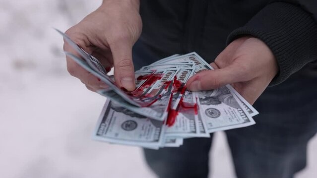 Criminal profits, Unethical income, Counting cash. A man's hands are calculating dollars that have been tainted with blood.