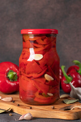 Fototapeta Pickled sweet peppers with garlic in glass jar on brown background, Vertical format obraz