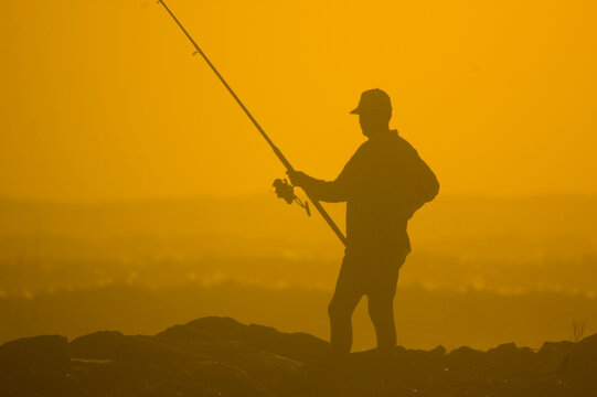 silhouette of a fisherman against a bright orange sky