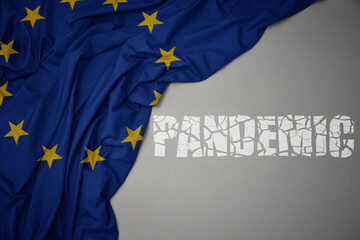 waving colorful national flag of european union on a gray background with broken text pandemic. concept.