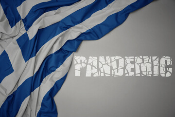 waving colorful national flag of greece on a gray background with broken text pandemic. concept.