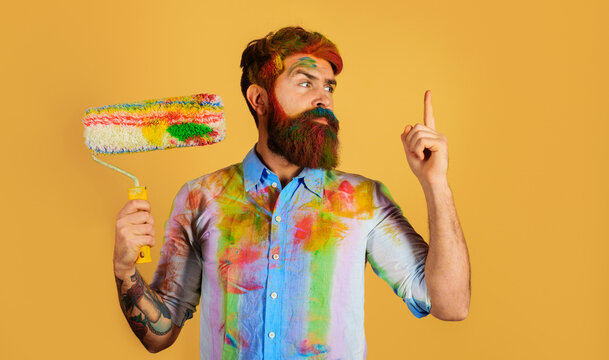 Painter with paint roller pointing finger up. Professional painter, decorator, builder worker with paintroller. Bearded worker with paint roller. Repairman or handyman in dye shirt with paint roller.