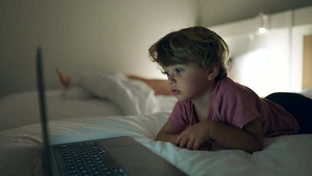 Small boy watching cartoons laying in bed at night. Child hypnotized by media online close up face in the evening