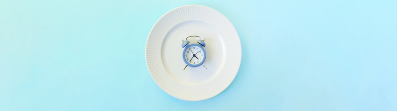 Intermittent fasting concept. Clock lay in the plate. Weight loss plan banner