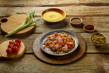 Israeli spice couscous with sumac and chicken pieces on a round wooden stand next to couscous, sumac and vegetables.
