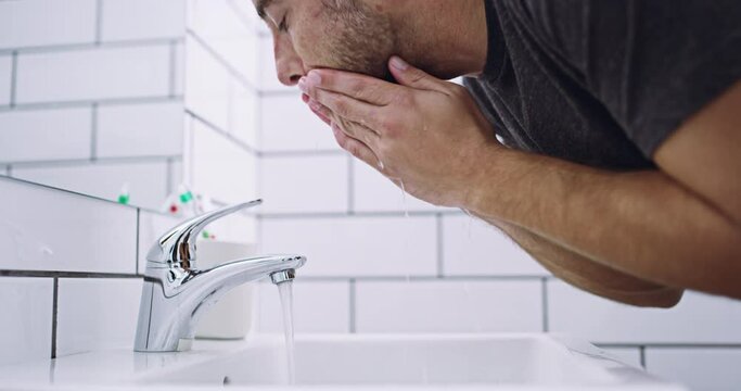 Man washing face, hygiene and skincare with water, basin and grooming during morning routine. Male person in bathroom, cleaning skin with hands and cleanliness, wellness and self care at home