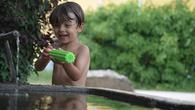 A joyful little boy smiling at laughing standing outside during summer day shirtless holding foam water toy gun. Candid and authentic smile and laugh