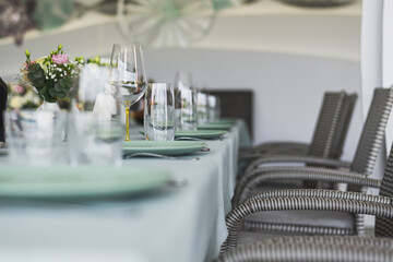 Wedding banquet. The festive table is decorated with compositions of flowers and greenery. On the table are glasses, talers with napkins, cutlery and name cards and menu cards.