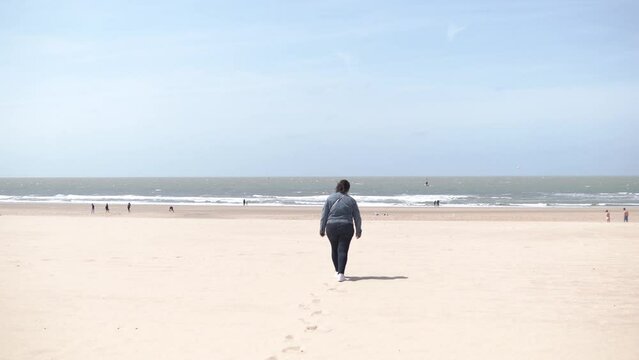 a woman walks along the beach in windy weather