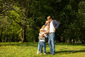 White Hugging Family. Mother, Father, Child Boy Stand In Park, Enjoying Time Together. Summer Time. Happy Parenthood, Family Leisure Time. Love And Care. Horizontal Plane