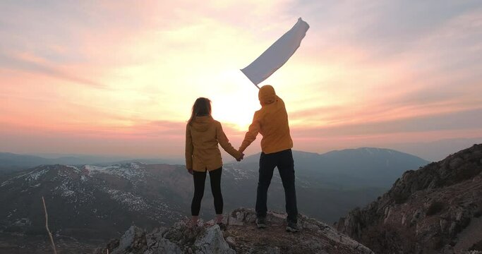 A man waving white flag holding a woman's hand against sunset dawn. Concept of peace and freedom