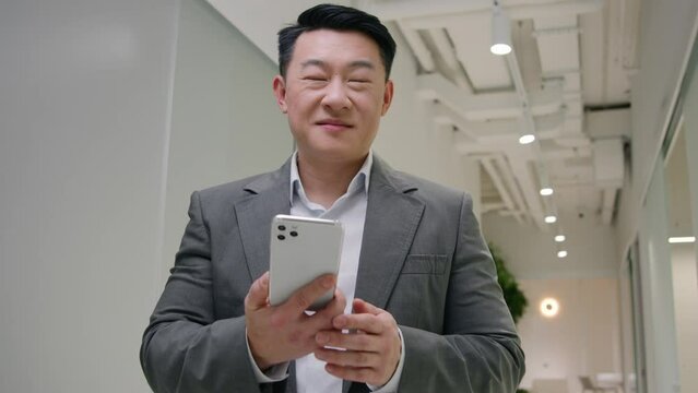 Asian middle-aged man businessman talk phone mobile conversation listen good news win business opportunity offer happy chinese korean entrepreneur office manager in hall smiling imagine success dream 