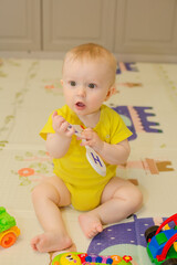 a baby boy in a yellow bodysuit is sitting on a children's rug next to toys