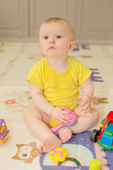 a baby boy in a yellow bodysuit is sitting on a children's rug next to toys