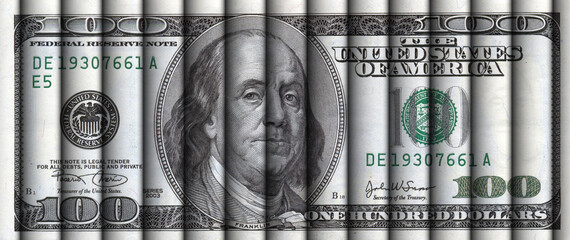 Rolls of hundred dollar bills aligned to display a one hundred dollar bill