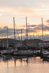 vertical photo of the marina at sunset full of sailboards, yachts, boats and vessels with reflections of clouds and sundown sky light