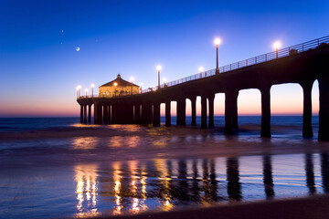 Fototapeta na wymiar Manhattan Beach California Pier at twilight. Moon and a few stars visible in the background. Pier lights reflecting on the sand.