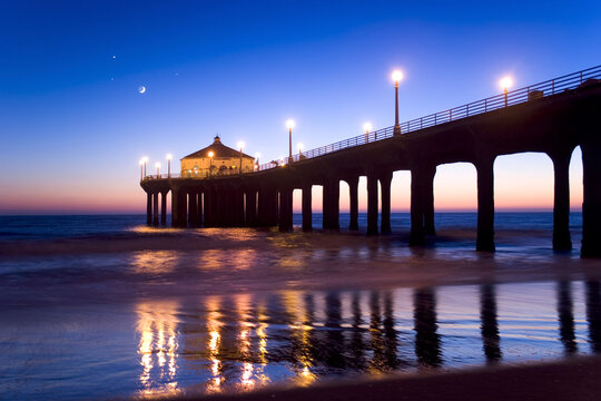 Manhattan Beach California Pier at twilight. Moon and a few stars visible in the background. Pier lights reflecting on the sand.