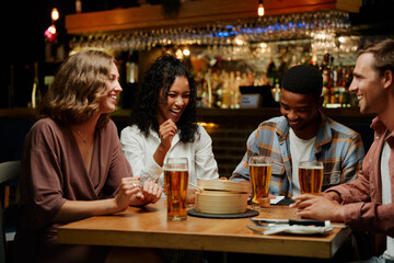 Happy young multiracial group of friends in casual clothing laughing over dinner at restaurant