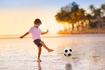 Kids play football on tropical beach at sunset