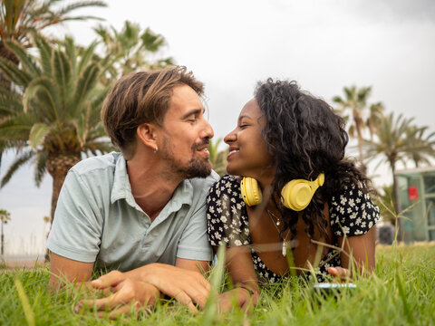 Diverse heterosexual couple affectionately lying on the grass of a park in a city