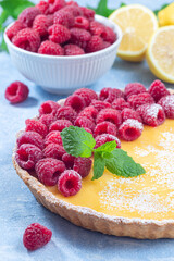 Lemon tart, garnished with fresh raspberry, icing sugar, mint, vertical