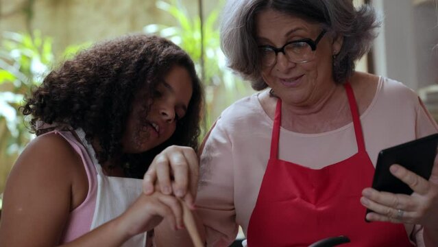 crian&ccedil;a latina na cozinha ajudando sua m&atilde;e e av&oacute; a fazerem brigadeiro seguindo uma receita no tablet no dia das m&atilde;es