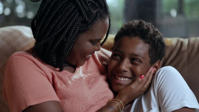 mulher negra barsileira sentada no sof&aacute; da sala abra&ccedil;ando e beijando seu filho no dia das m&atilde;es