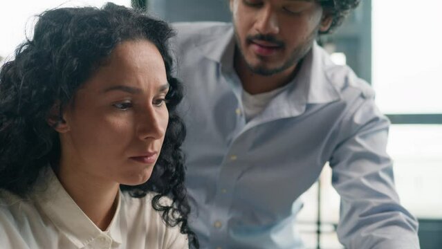 Leader mentor Indian Arabian man boss teach intern help woman with laptop program check documents in office multiracial businessman and businesswoman solve difficulties together business discussion 