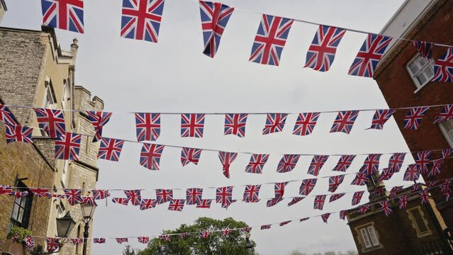 Handheld shot several strings uk flags union jacks hanging between buildings following the coronation of King Charles