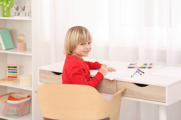 Naklejka premium Little boy drawing at desk in room. Home workplace