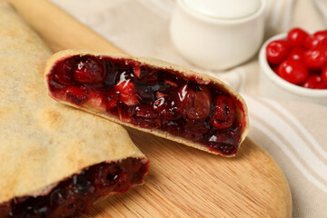 Delicious strudel with cherries on wooden board, closeup
