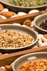 Coriander seeds and various spices close up in a wooden tray.