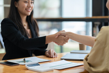 Two asian businesswoman shaking hands in modern office after success in financial business Documents investing in teamwork and friendship. startup business ideas real estate project.