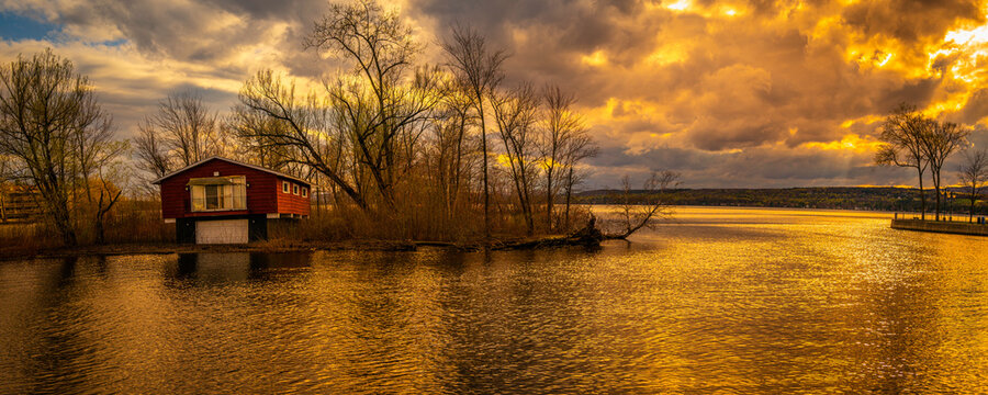 Charest Island and abandoned house in Magog Bay next to Ponte-Merry Park in Quebec, Canada, and dramatic cloudscape in the sky at golden sunset
